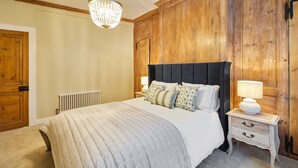 Une chambre à coucher avec un grand lit, des lambris en bois aux murs, un lustre et une table de chevet avec une lampe.