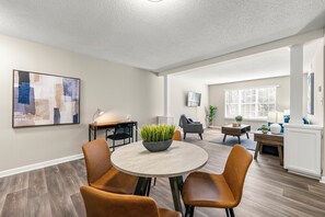 Un salon moderne avec une table ronde, deux fauteuils en cuir marron, un canapé gris et une table basse agrémentée d’une plante.