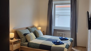 A bedroom with a bed, nightstand, lamp, window with curtains, and a radiator. - Apartmá Beatrice (Brno)