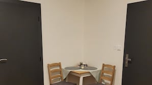A small room with two wooden chairs and a table, a dark door on one side, and a white wall. - Apartmá Beatrice (Brno)