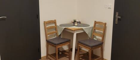 A small room with two wooden chairs and a table, a dark door on one side, and a white wall.