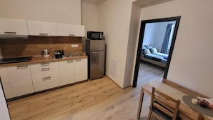 A modern kitchen with white cabinets, a stainless steel refrigerator, and a microwave. There is a wooden dining table with chairs. - Apartmá Beatrice (Brno)