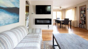 A living room with a sofa, a flat-screen TV mounted on the wall, a dining table with chairs, and a bookshelf. - 1st flr nr Shaker, RTA rail, Cle Clinic & Univ. Ho (Akron)