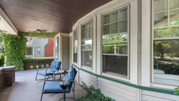 Ein überdachter Balkon mit zwei Stühlen und einem Tisch, großen Fenstern und Bepflanzung an den Wänden.