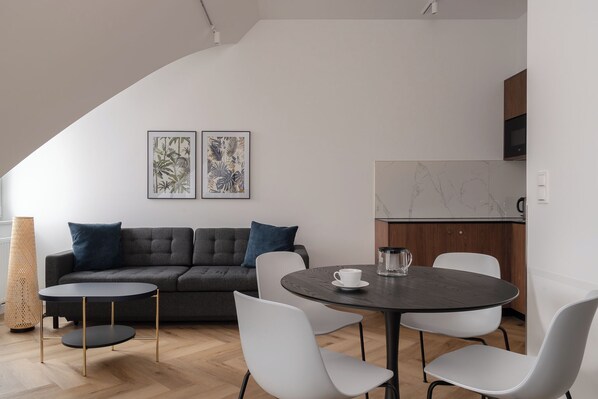 A modern living space with a dark grey sofa, white chairs, a round table, and two framed botanical prints on the wall. - RentPlanet - Przy Ogrodzie Botanicznym (Wroclaw)