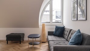 A modern living room with a grey sofa, two blue cushions, a round black table with gold legs, and a tall woven floor lamp. - RentPlanet - Przy Ogrodzie Botanicznym (Wroclaw)