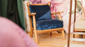 Una silla de madera con un cojín oscuro en una habitación con papel tapiz floral y piso de madera.