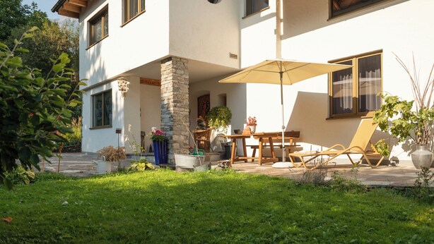 Una casa de dos pisos con un patio que incluye una mesa, sillas y una sombrilla.