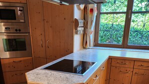 Una cocina con armarios de madera, horno empotrado, estufa y ventana con vistas al verdor.