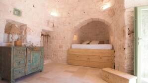 Quarto rústico com parede de pedra, cama de madeira, cômoda de madeira e um banco.