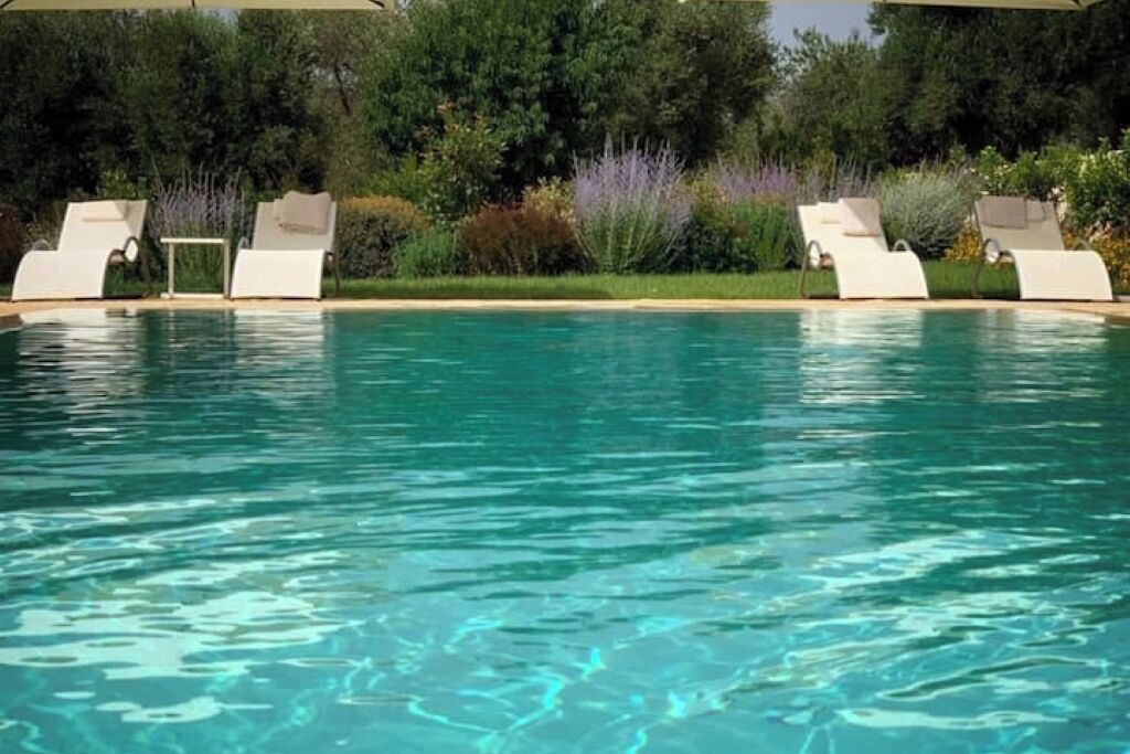 Une piscine à l’eau cristalline, entourée de chaises longues blanches et d’une végétation luxuriante.