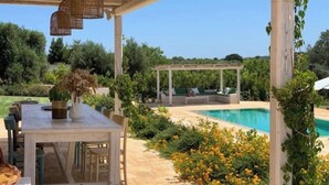 Uma área externa coberta com piscina, mesa e cadeiras, e um pergolado.