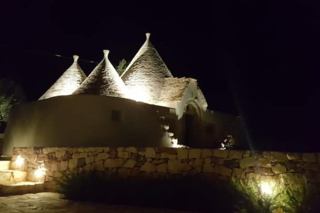 A building with a stone facade and multiple pointed roofs, illuminated by exterior lighting.