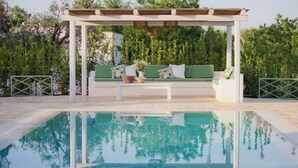 Uma piscina com pérgola branca e área de estar com assentos verdes.