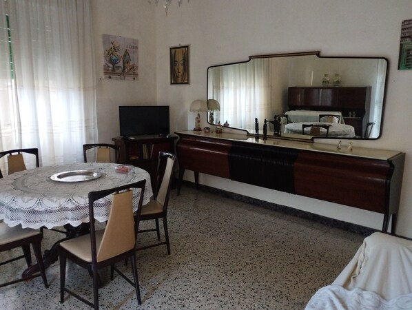 A compact hotel room with a dining area featuring a round table and chairs, a small television, a mirror, and a kitchenette with a sink and countertop. - Naples Fuorigrotta stadium Maradona building video monitored apartment 85 sqm (Napoli)