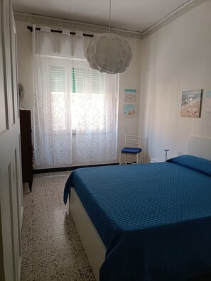 A bedroom with a bed, a chair, a window with curtains, and wall decorations. - Naples, Fuorigrotta, Maradona Stadium, Building with Video Surveillance, 85 sqm Apartment (Napoli)