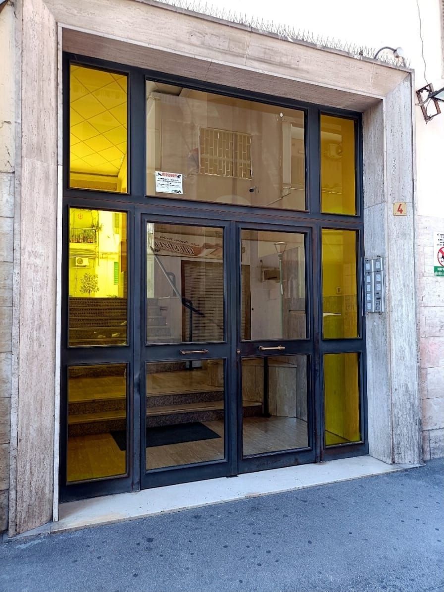 A building entrance with a large glass door, a sign above the door, and a number '4' on the wall to the right.