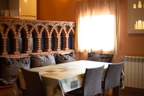 A dining area with a brick wall, a table with chairs, and a window with curtains. - 2 Bedroom Apartment Africa (Munébrega)
