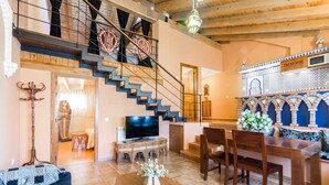 Amplia sala de estar con una escalera de madera, un televisor y un comedor con una pared decorativa.