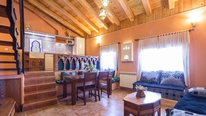 Una sala de estar acogedora con una escalera de madera, un comedor con mesa y sillas, y un sofá con cojines estampados.