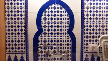 Un baño con azulejos blancos y azules estampados, una ducha de diseño curvo y un enchufe visible.