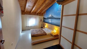 A bedroom with a wooden ceiling, a bed with a patterned bedspread, bedside lamps, and a large wall mural of a mountain landscape. - 2 Bedroom Apartment Asia (Munébrega)