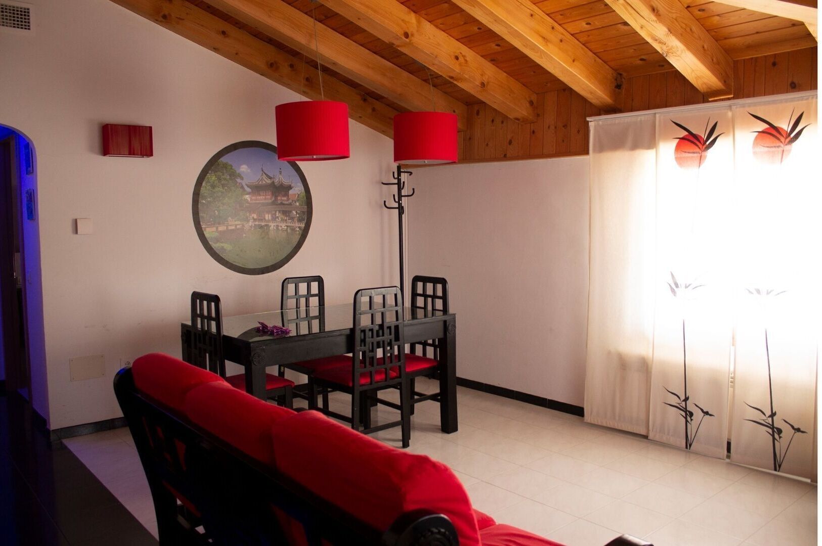 Un espace repas doté d’un plafond en bois, d’une table ronde entourée de chaises et de lampes rouges.