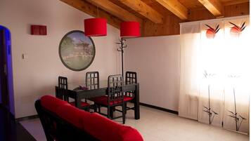 Un espace repas doté d’un plafond en bois, d’une table ronde entourée de chaises et de lampes rouges.