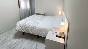 Une petite chambre à coucher, bien rangée, avec un lit, une table de chevet et une commode.