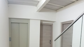 Un corridoio con ringhiera in vetro, una porta in legno e un pavimento chiaro.