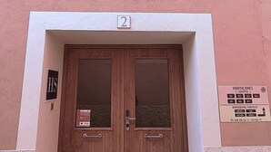 Una porta in legno a due ante con un piccolo oblò, il numero '2' sopra e una segnaletica che indica alloggi alberghieri con numeri di stanza e un numero di telefono.