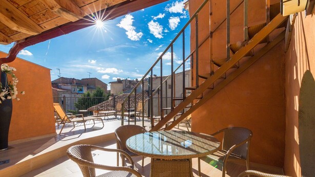 Patio esterno luminoso con mobili in vimini e tavolo in vetro, con vista sulla città.