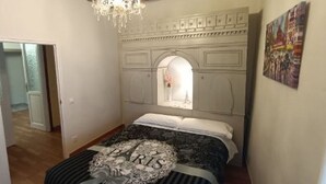 A bedroom with a bed, a chandelier, a window with a view, and a painting on the wall. - Two bedroom apartment (Munébrega)