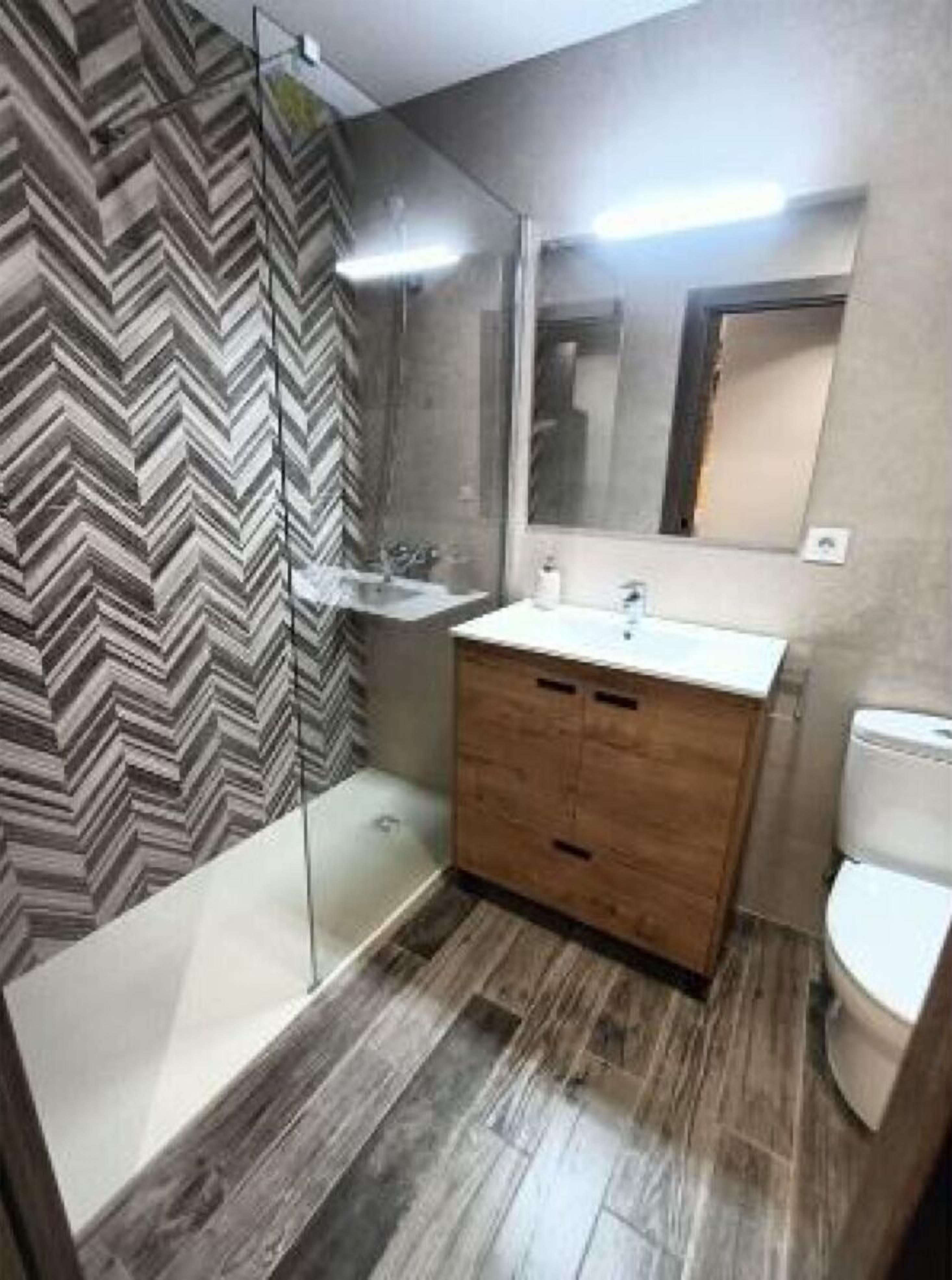 Ein modernes Badezimmer mit einer Wand im Zickzack-Muster, einem Holz-Waschtisch, einer Glasdusche und einer Toilette.