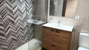 Ein modernes Badezimmer mit einer Wand im Zickzack-Muster, einem Holz-Waschtisch, einer Glasdusche und einer Toilette.