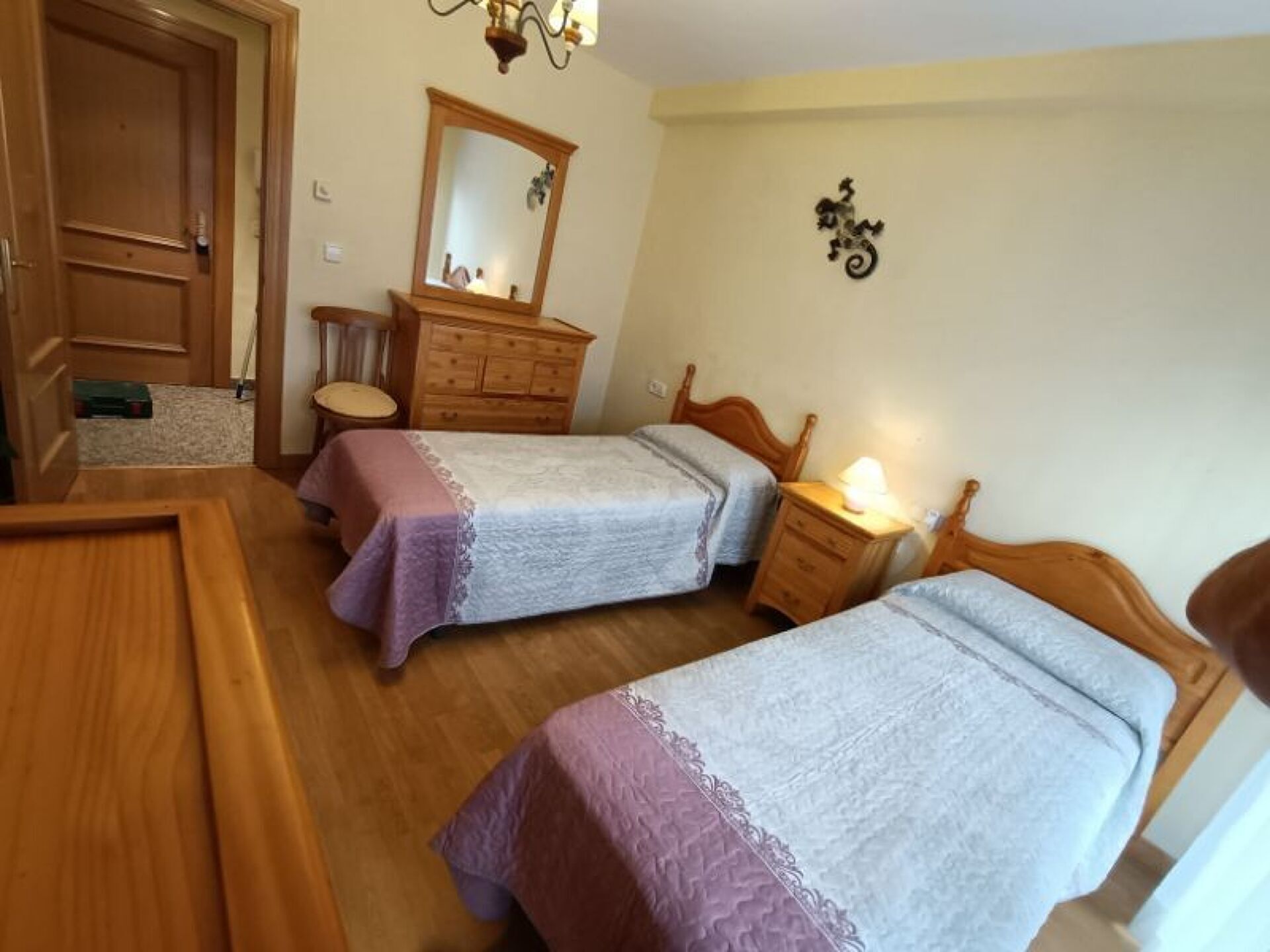 A bedroom with two single beds, a wooden dresser, a mirror, and a small table with a lamp.