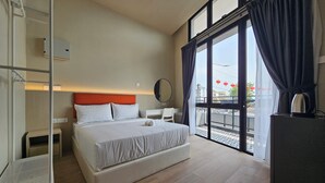 A hotel room with a large bed, a desk, a chair, a wardrobe, and a balcony with a view of the city. - Room at Weld Quay Georgetown (George Town)