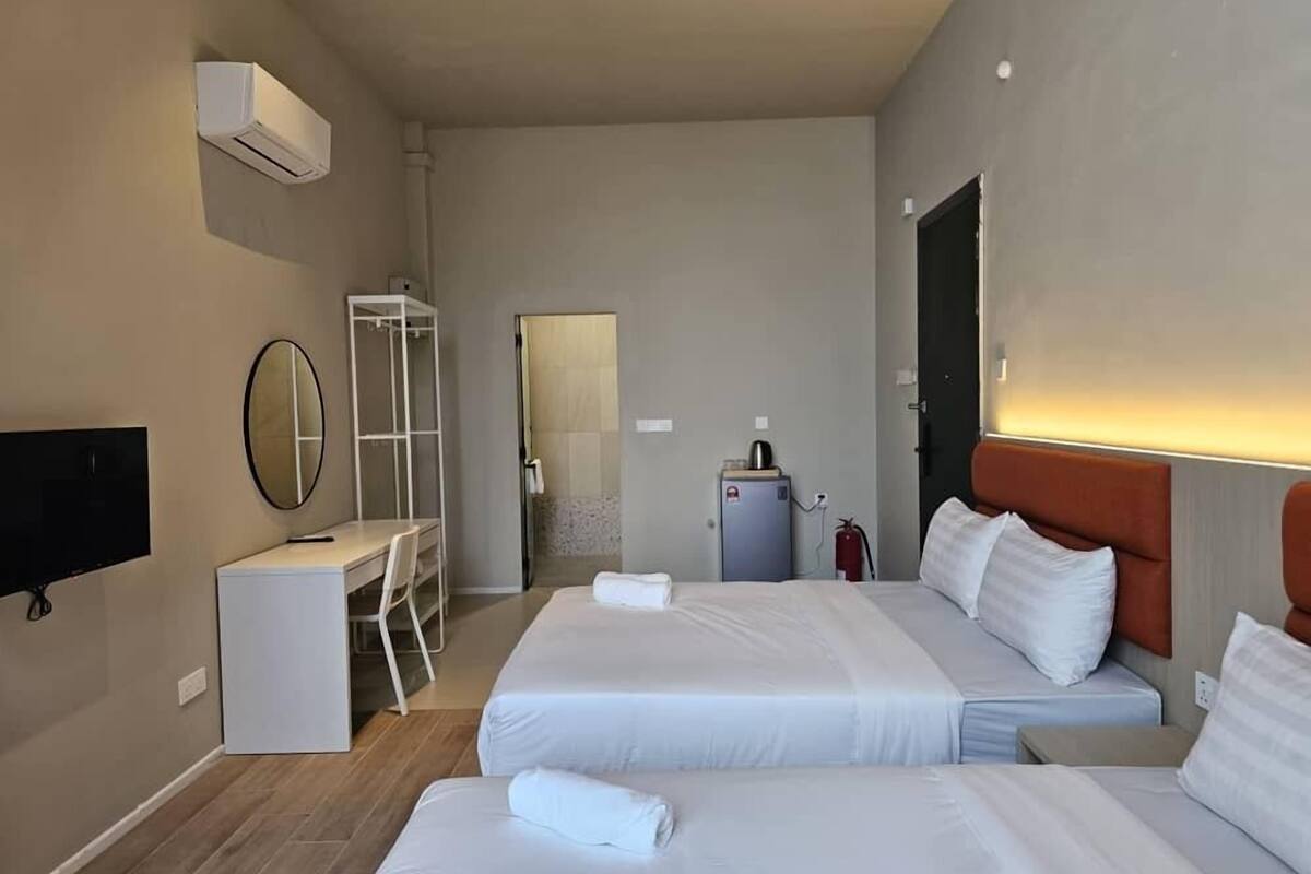 A hotel room with two beds, a desk, a chair, a mirror, an air conditioning unit, and a fire extinguisher.