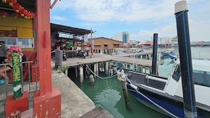 A pier with boats docked, a restaurant with outdoor seating, and a view of the water and city skyline. - Room at Weld Quay Georgetown (George Town)