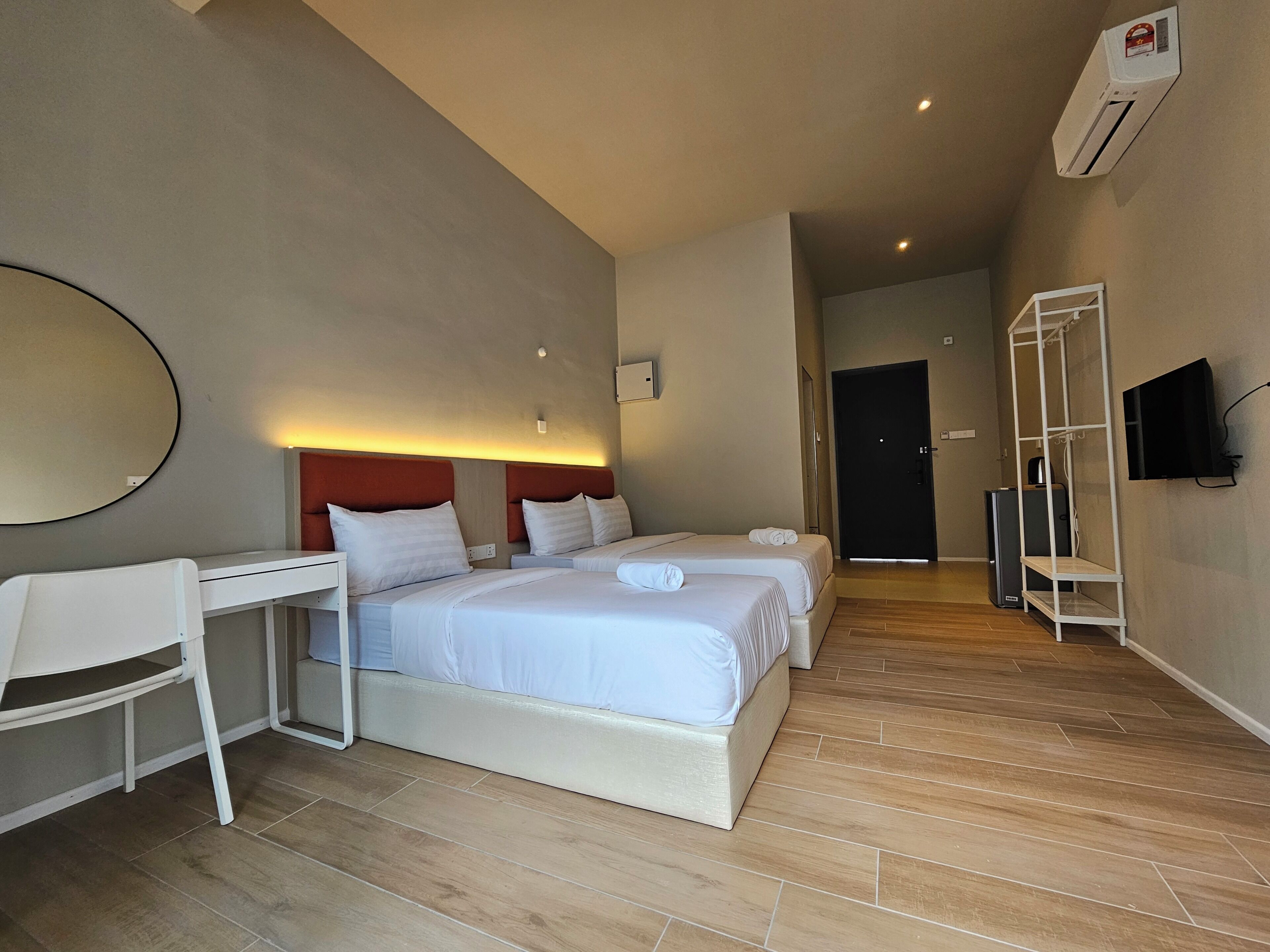 A hotel room with two beds, a desk, a chair, a TV, and an air conditioning unit.