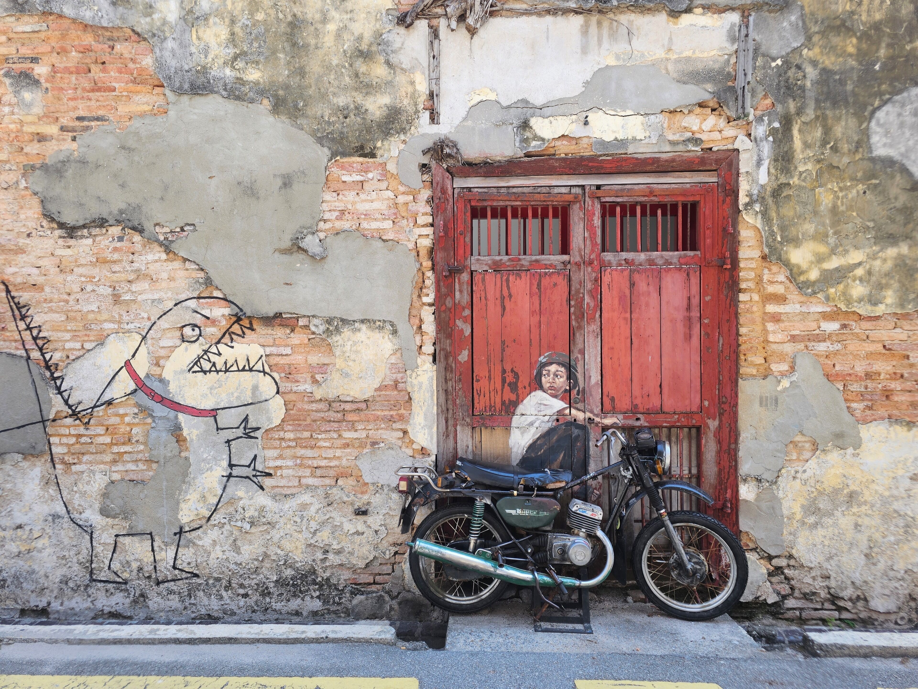 A motorcycle parked in front of a weathered building with a red door and a mural on the wall.