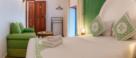 A hotel room with a bed, a green sofa, a small table, and a door.