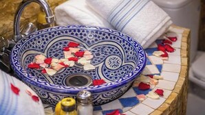 A bathroom sink with a blue and white patterned basin, a faucet, and scattered rose petals. - Riad Rayahana Fes (Fes)
