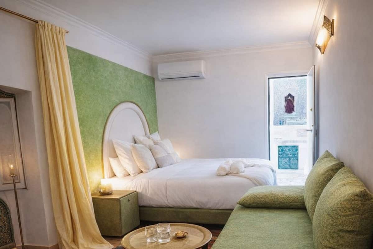 A hotel room with a bed, a green sofa, a small round table, and a window with a view.