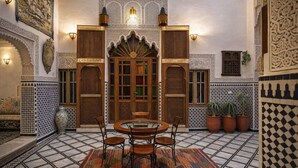 A traditional Moroccan interior with a tiled floor, ornate wooden doors, and a round table with chairs. - Riad Rayahana Fes (Fes)