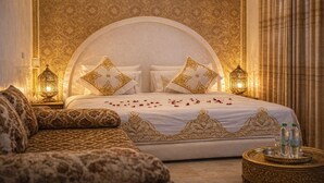 A luxurious bedroom with a large bed, ornate pillows, a patterned sofa, and decorative wall and floor tiles. - Riad Rayahana Fes (Fes)