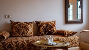 A cozy living room with patterned cushions, a small round table with salt and pepper shakers, a wall-mounted light, and a mirror. - Riad Rayahana Fes (Fes)