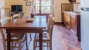 A dining area with a brick ceiling, a wooden table, and chairs. There is a television and a kitchen visible in the background. - Ground floor apartment with one double bedroom (Toscana)