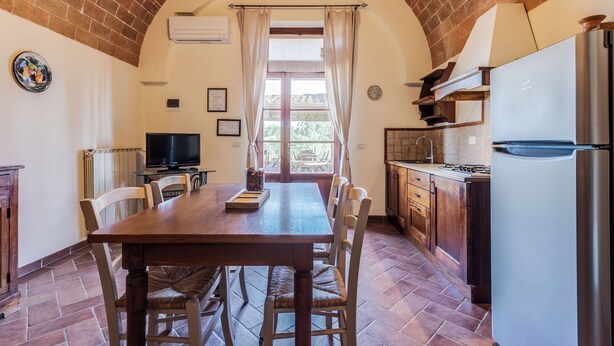 A spacious kitchen with a large wooden table, modern appliances, and a brick arch ceiling. - Ground floor apartment with one double bedroom (Toscana)