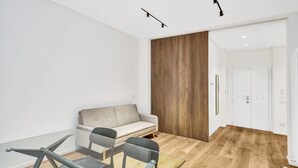 A modern room with a glass table, grey chairs, a grey sofa, and a wooden accent wall.